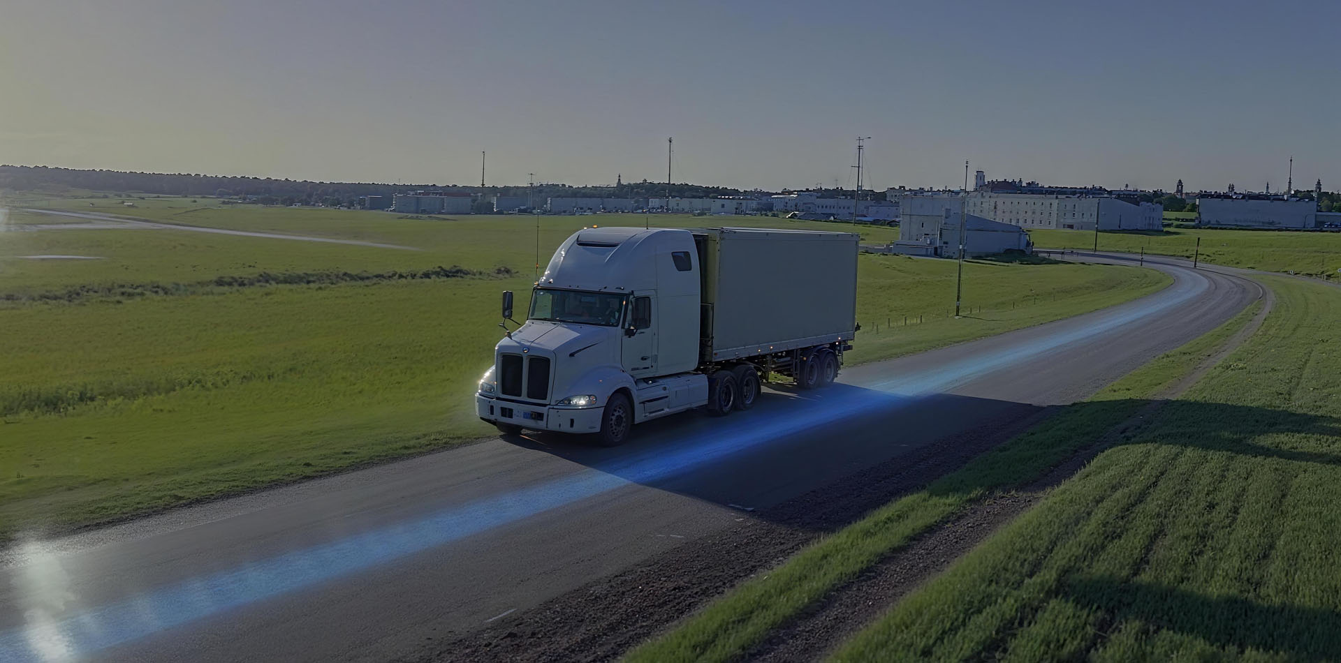 White semi truck driving along a rural road through open green fields